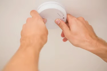 Hands fitting a smoke alarm to a ceiling